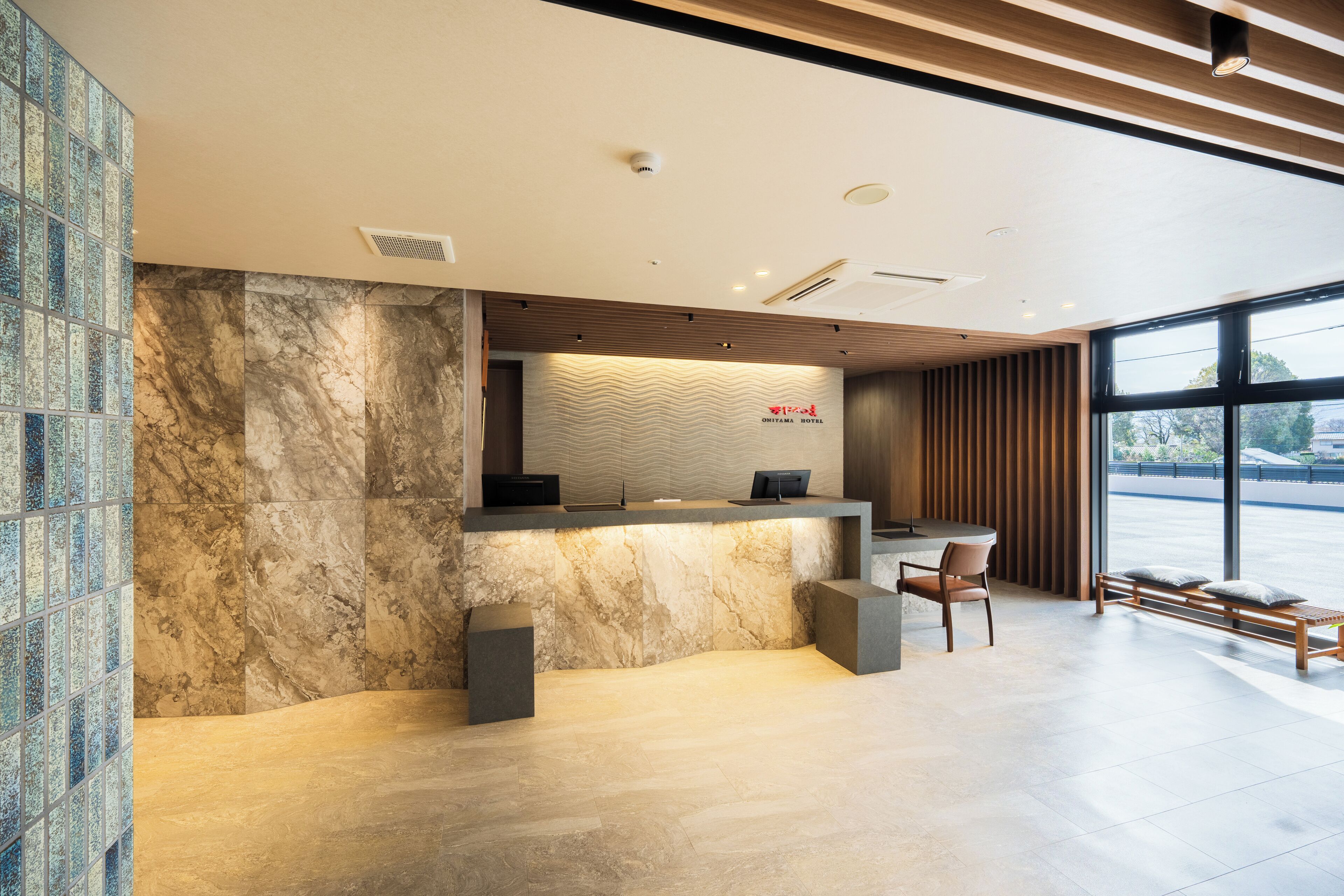 A modern hotel reception area with a marble reception desk, seating, and large windows offering a view.