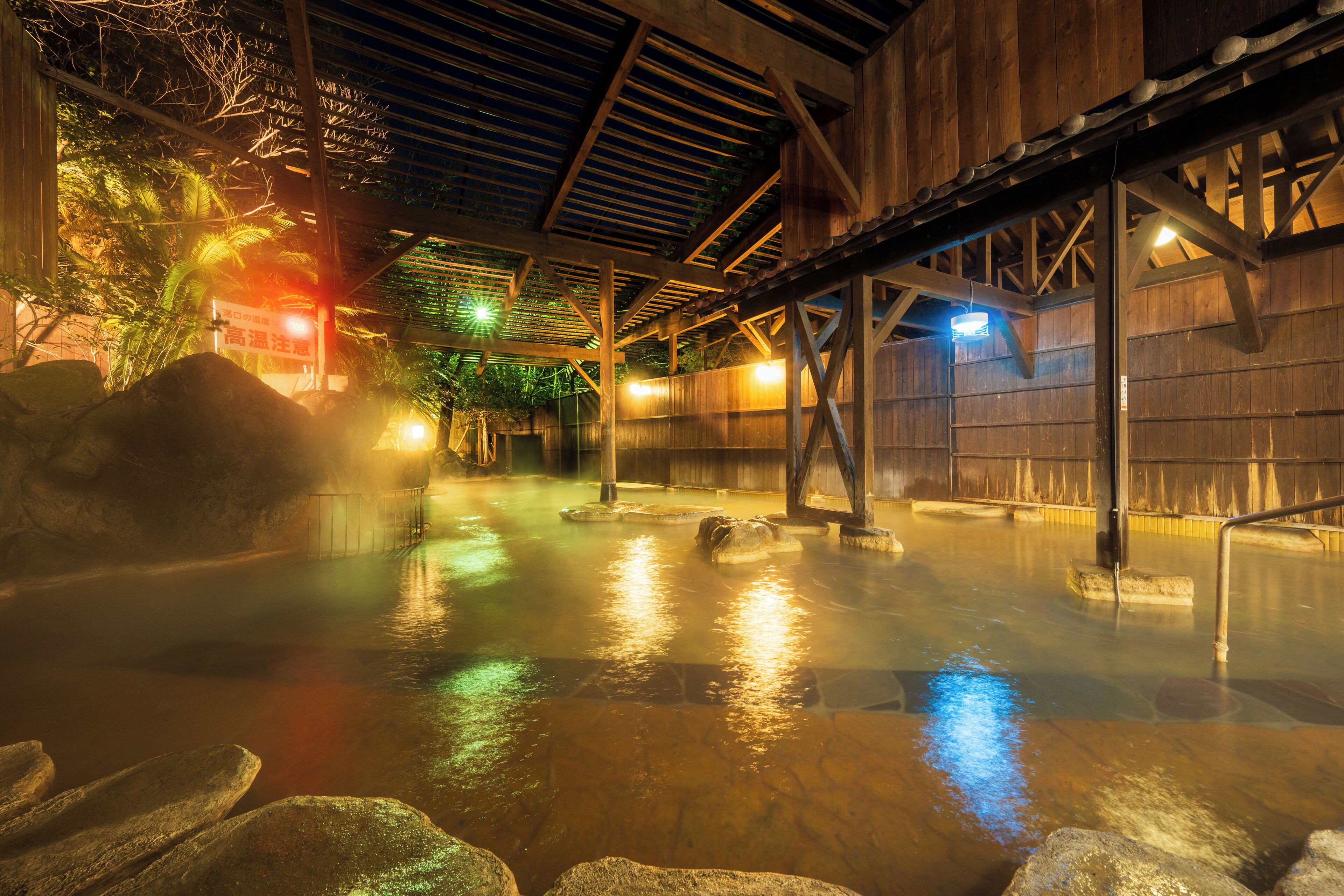 A hot spring area with wooden beams, rocks, and a wooden wall.