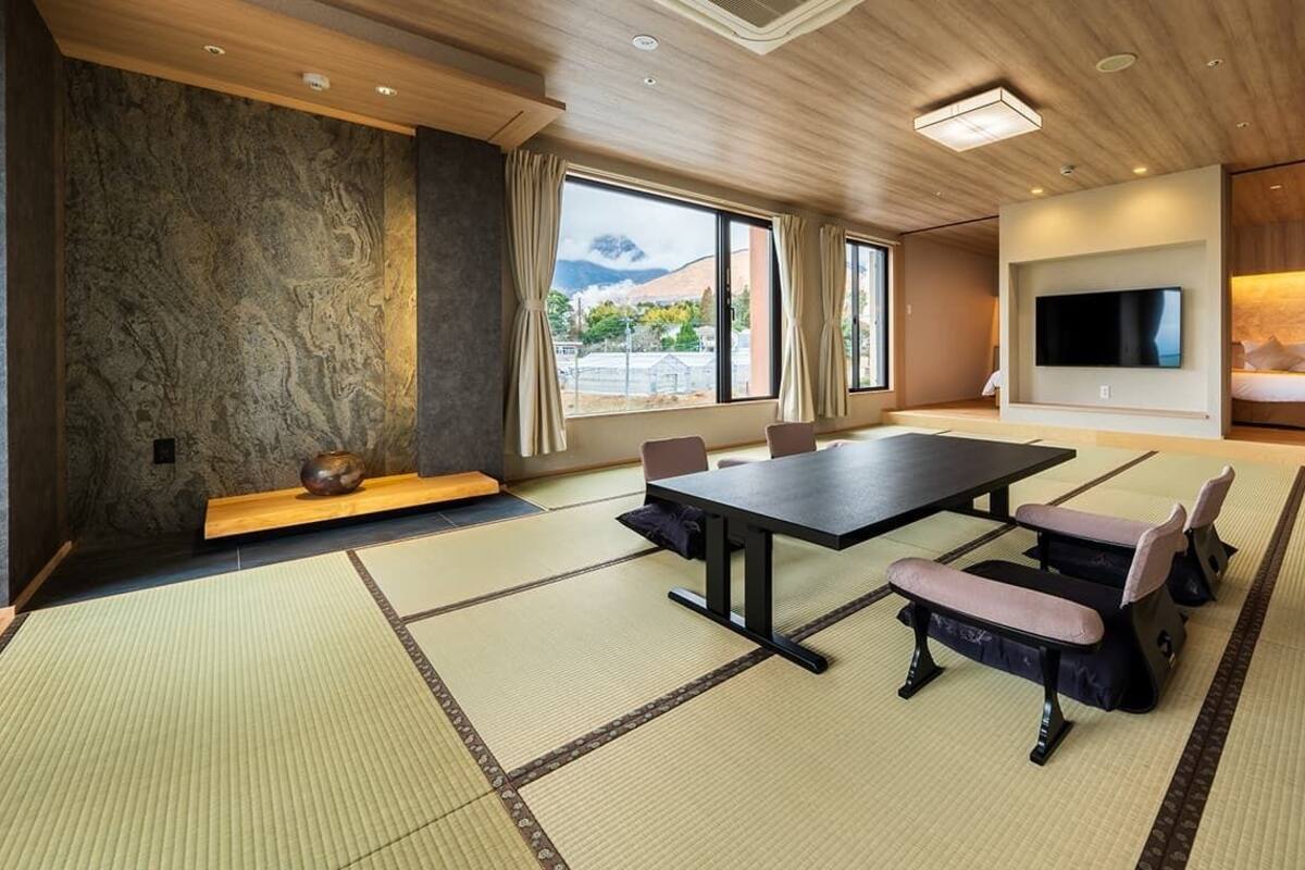 A modern hotel room with tatami mats, a dining table, a TV, and a bed.