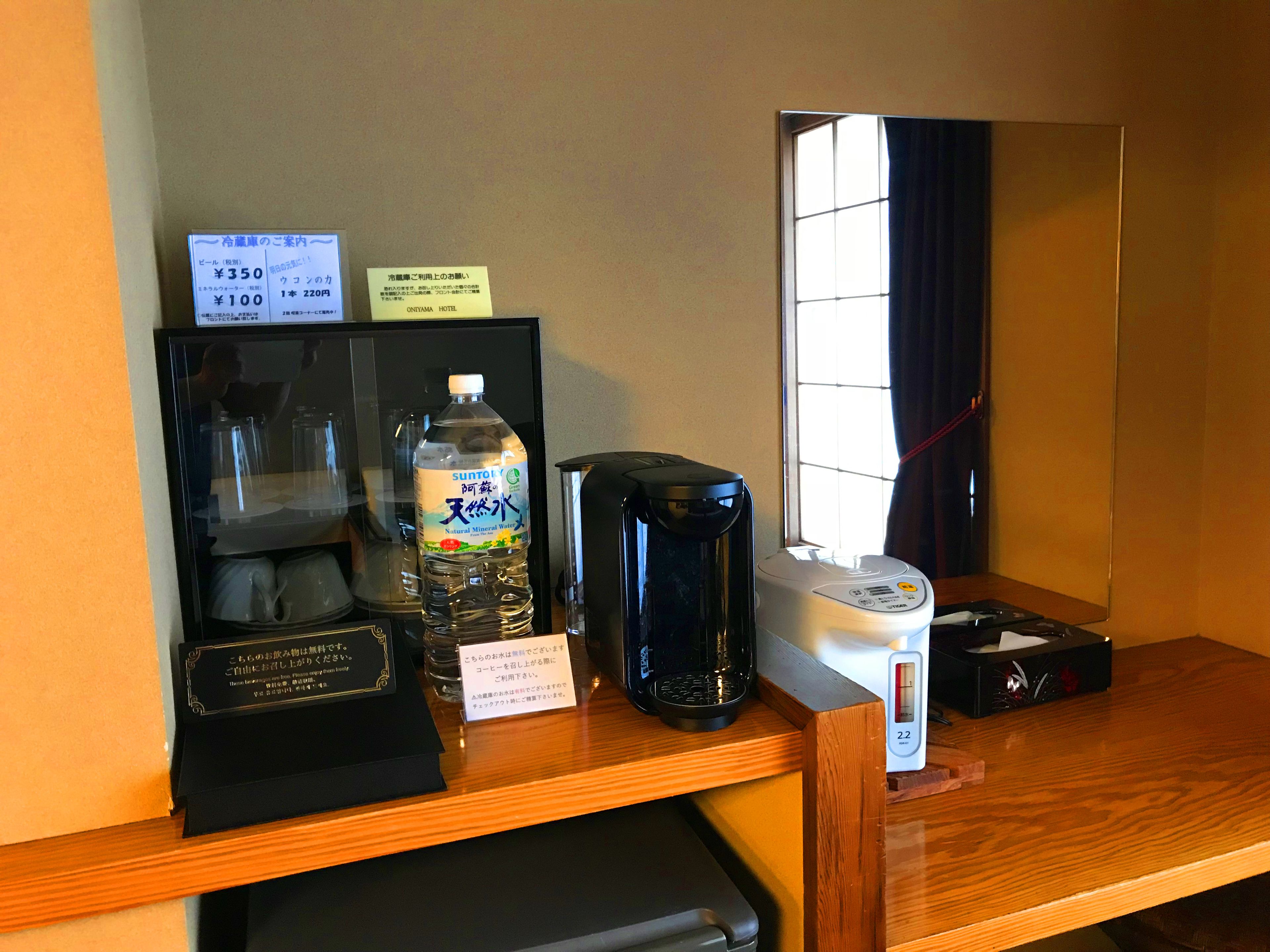 A hotel room with a wooden desk, a coffee maker, a water bottle, and a digital scale.