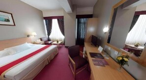 Una habitación de hotel con cama, escritorio, silla, televisor y espejo.