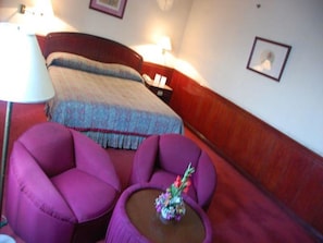 A hotel room with a bed, two purple armchairs, a small table with a vase, and a nightstand with a lamp. - Great Eastern Hotel Quezon City (Quezon City)