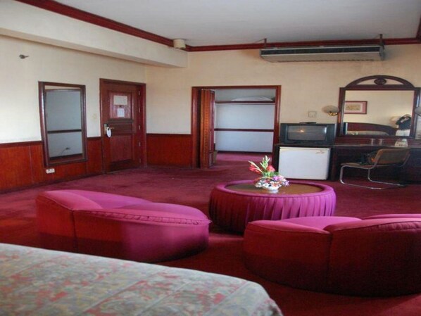 A hotel room with a large bed, a desk with a computer, a television, and a small table with flowers.