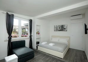 A modern bedroom with a bed, a sofa, a window with curtains, a wall-mounted air conditioner, and a flat-screen TV. - Candia Green House B&B (Rome)