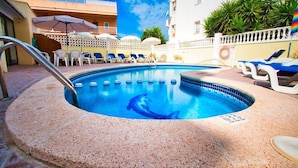 A swimming pool with a dolphin, surrounded by lounge chairs and umbrellas, with buildings in the background. - Bon Aire Apartamentos (Calvia)