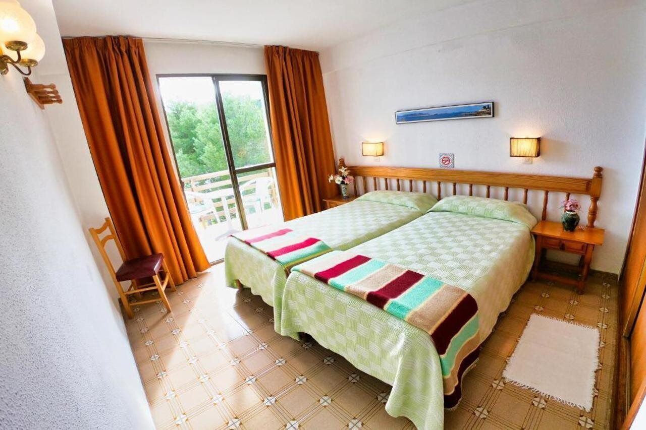 Una cama doble con cabecera de madera, dos mesitas de noche con lámparas, una silla y vistas a zonas verdes.