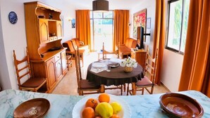 A dining area with a round table set for four, surrounded by wooden chairs. A fruit bowl with oranges and lemons is on the table, and there is a wooden cabinet to the left. - Bon Aire Apartamentos (Calvia)