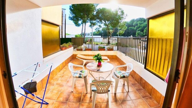 A balcony with a table and chairs, potted plants, and a view of trees and a road. - Bon Aire Apartamentos (Calvia)