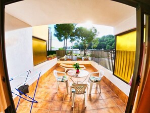 A balcony with a table and chairs, potted plants, and a view of trees and a road.