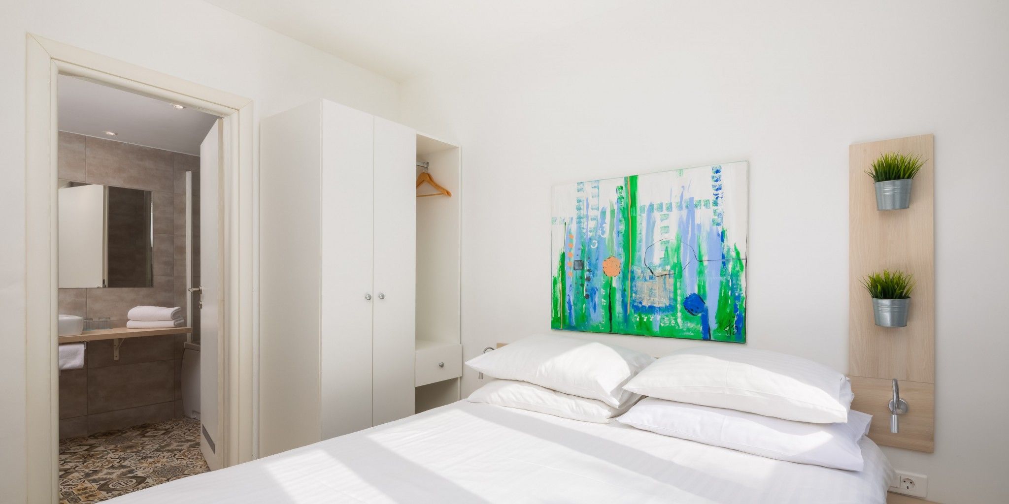 Un dormitorio moderno con una cama, un cuadro y una pequeña planta en la pared.