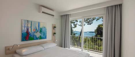 A bedroom with a bed, a painting, an air conditioning unit, and a balcony with a view.