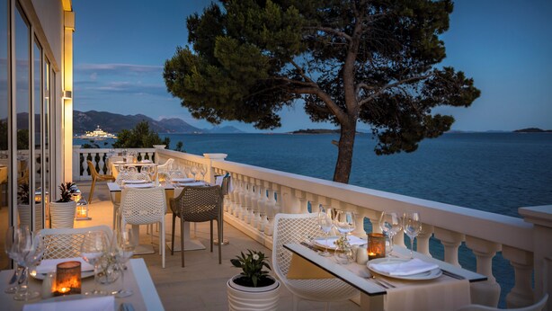 An outdoor dining area with tables set for two, overlooking a body of water and mountains. - Bellevue Maradiso Casa by Aminess (Orebic)