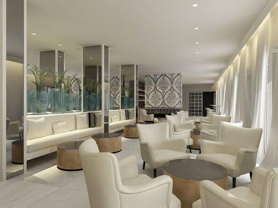 A modern lounge area with white furniture, a patterned wall, and a large window with sheer curtains.