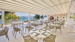 An outdoor dining area with round tables and wicker chairs, overlooking a scenic view of the sea and hills. - Bellevue Maradiso Casa by Aminess (Orebic)