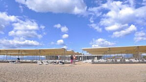 Une plage avec des parasols et des chaises longues, une personne qui se promène et un bâtiment en arrière-plan.