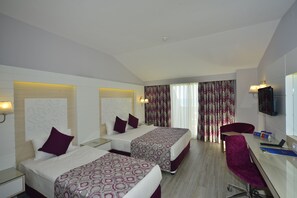 Habitació d'hotel amb dos llits, una taula, una cadira, un televisor i una finestra amb cortines.