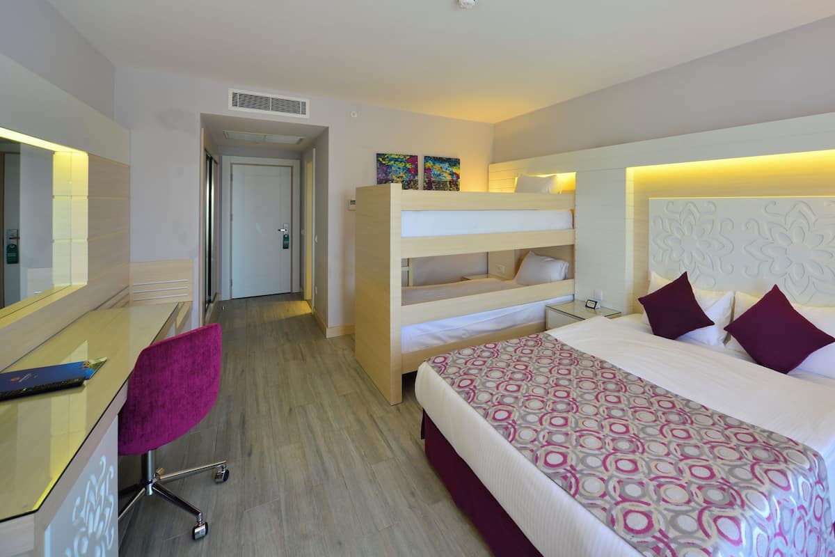 Une chambre d’hôtel avec un lit superposé, un bureau avec une chaise, une table de chevet avec une lampe et un téléphone.