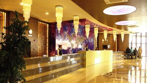 Een hotellobby met een receptiebalie, een grote decoratieve wand en een plant.