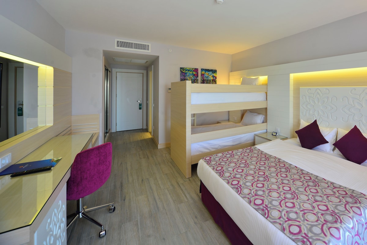 Ein Hotelzimmer mit einem Etagenbett, einem Schreibtisch mit Stuhl, einem Nachttisch mit Lampe und einem Telefon.