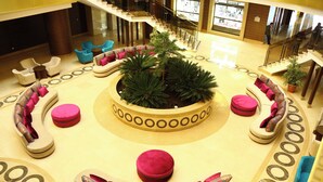 Un espace de détente circulaire, avec une plante au centre, entouré de canapés et de poufs, et un escalier en arrière-plan.