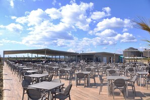An outdoor café with numerous tables and chairs, a covered seating area, and a view of the sea and buildings in the background. - Sunmelia Beach Resort Hotel & SPA (Manavgat)