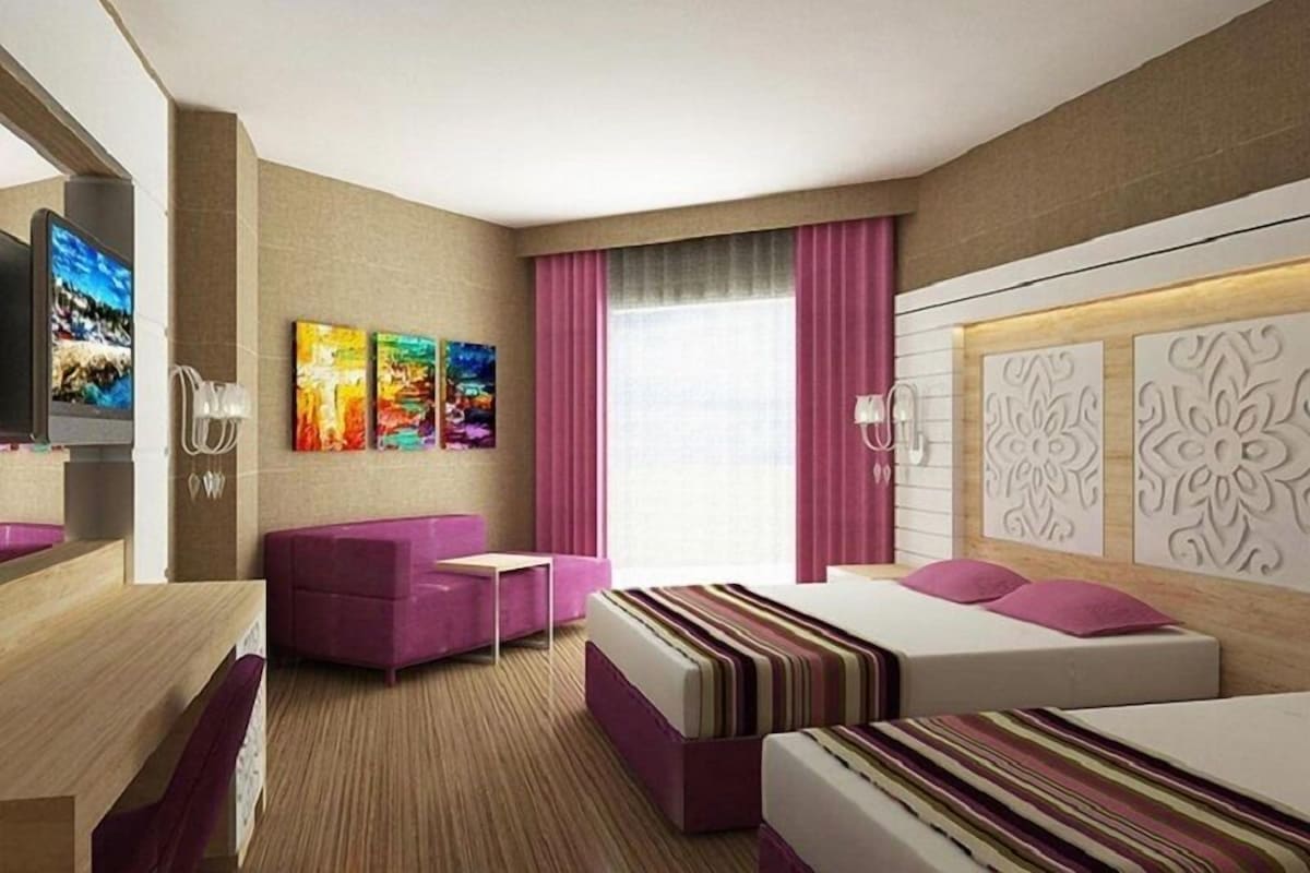 A hotel room with a bed, a sofa, a TV, and artwork on the wall.