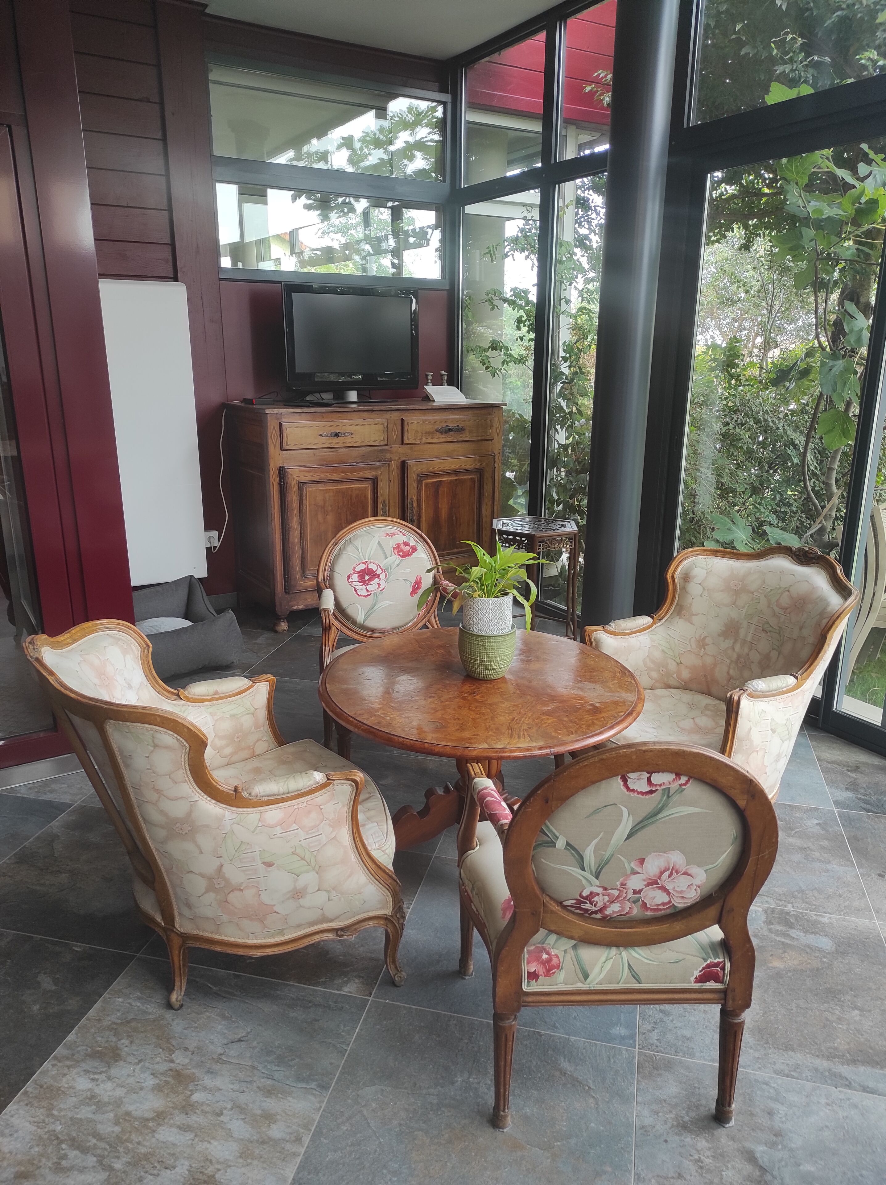 Un comedor con una mesa redonda de madera, sillas tapizadas con motivos florales y un mueble con un televisor.