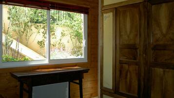 Een kamer met een houten bureau, een bed en een raam met uitzicht op een tuin.