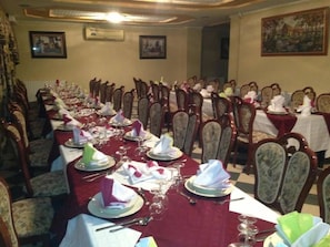 A banquet hall with long tables set for a formal event, wooden chairs, and framed pictures on the walls. - Frantz Fanon (Setif)