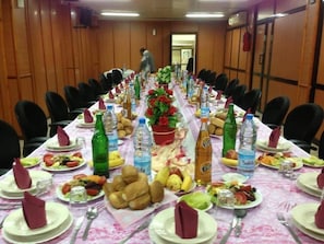 A conference room with a long table set for a meeting, equipped with chairs, plates, cutlery, and bottled water. - Frantz Fanon (Setif)