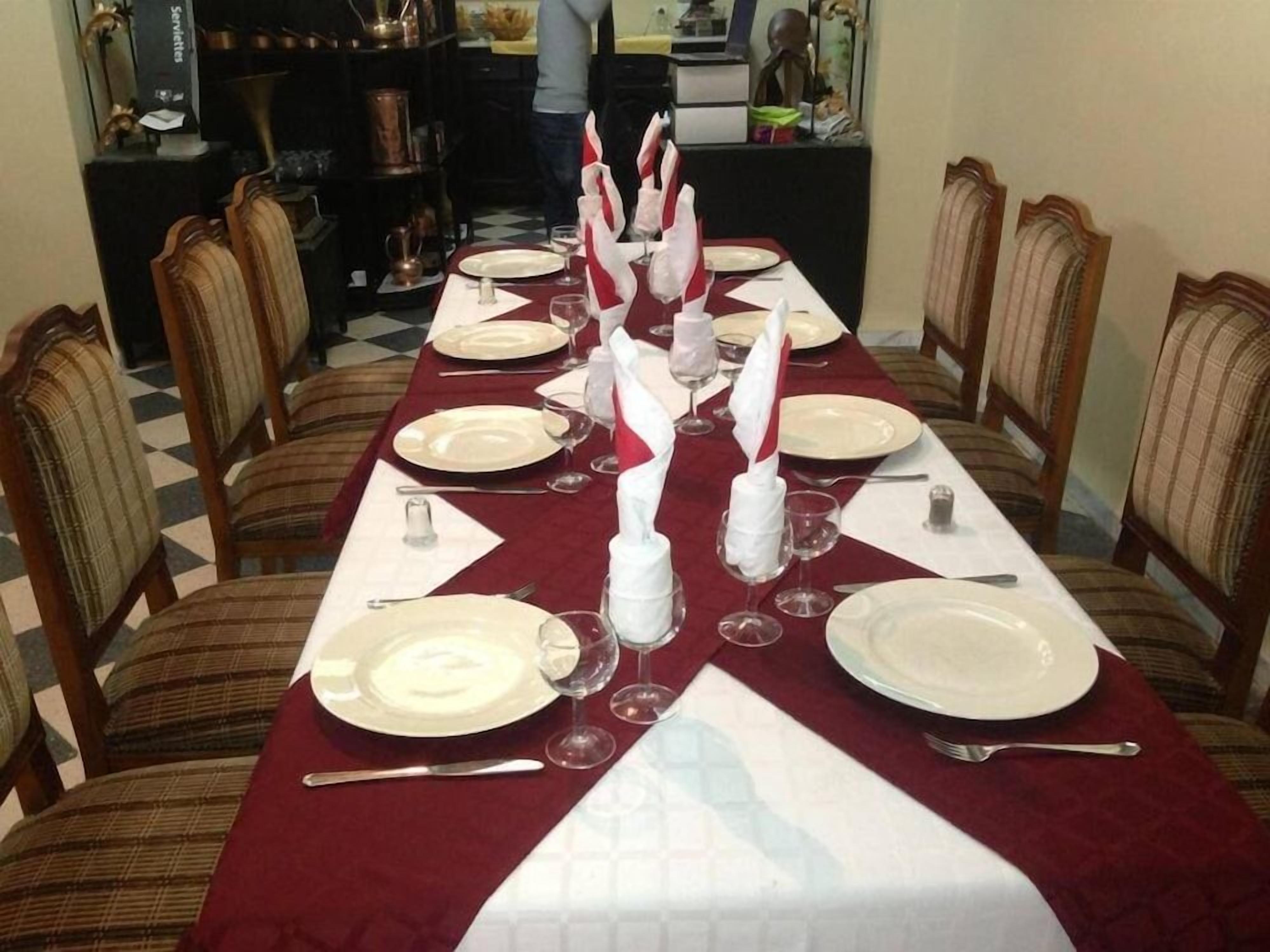 Une table à manger dressée avec de l’argenterie blanche, des couverts et des verres à vin, recouverte d’une nappe rouge et agrémentée de serviettes blanches.