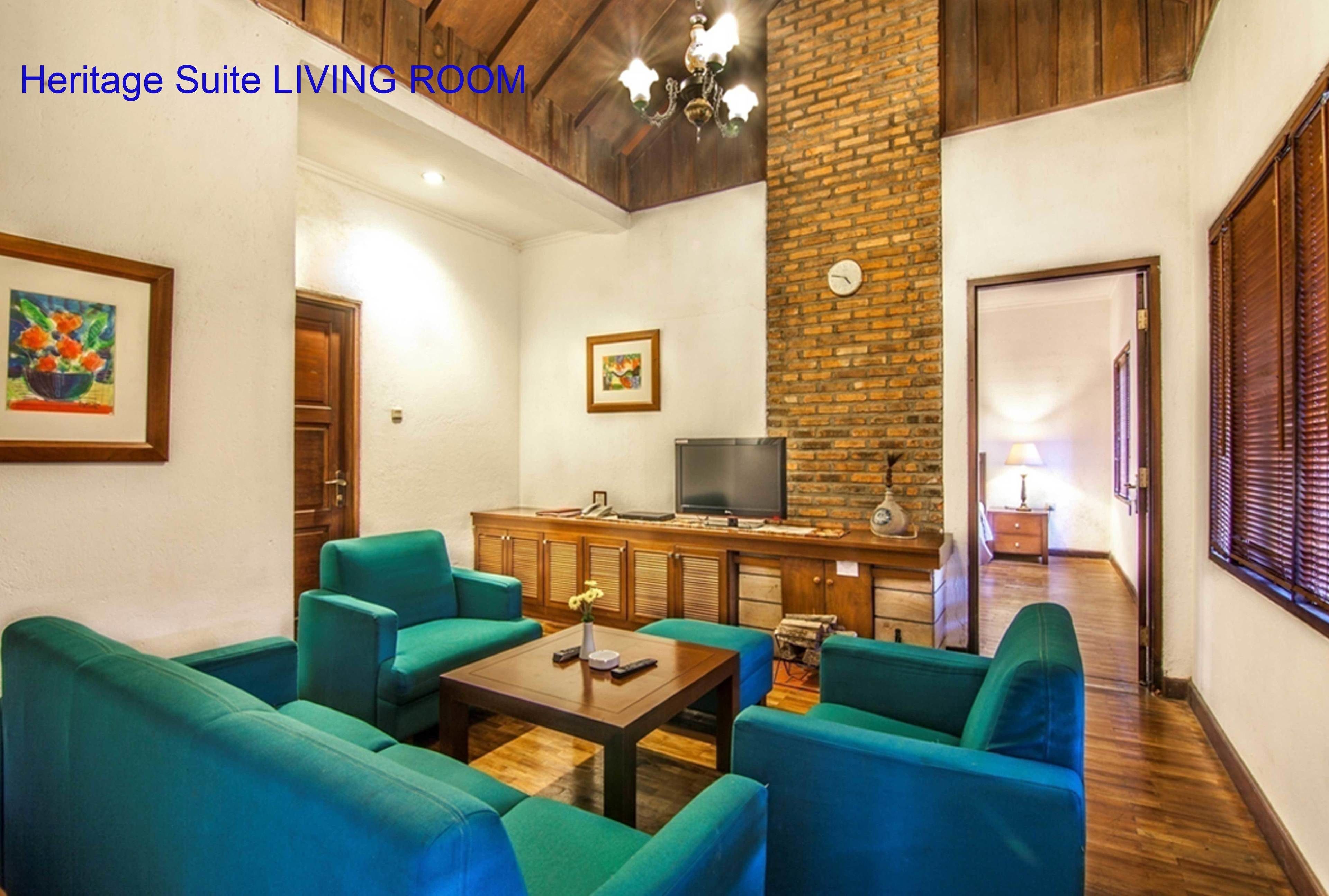A Heritage Suite living room with teal sofas, a wooden coffee table, a brick accent wall, and a television on a wooden cabinet.