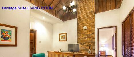 A Heritage Suite living room with teal sofas, a wooden coffee table, a brick accent wall, and a television on a wooden cabinet.