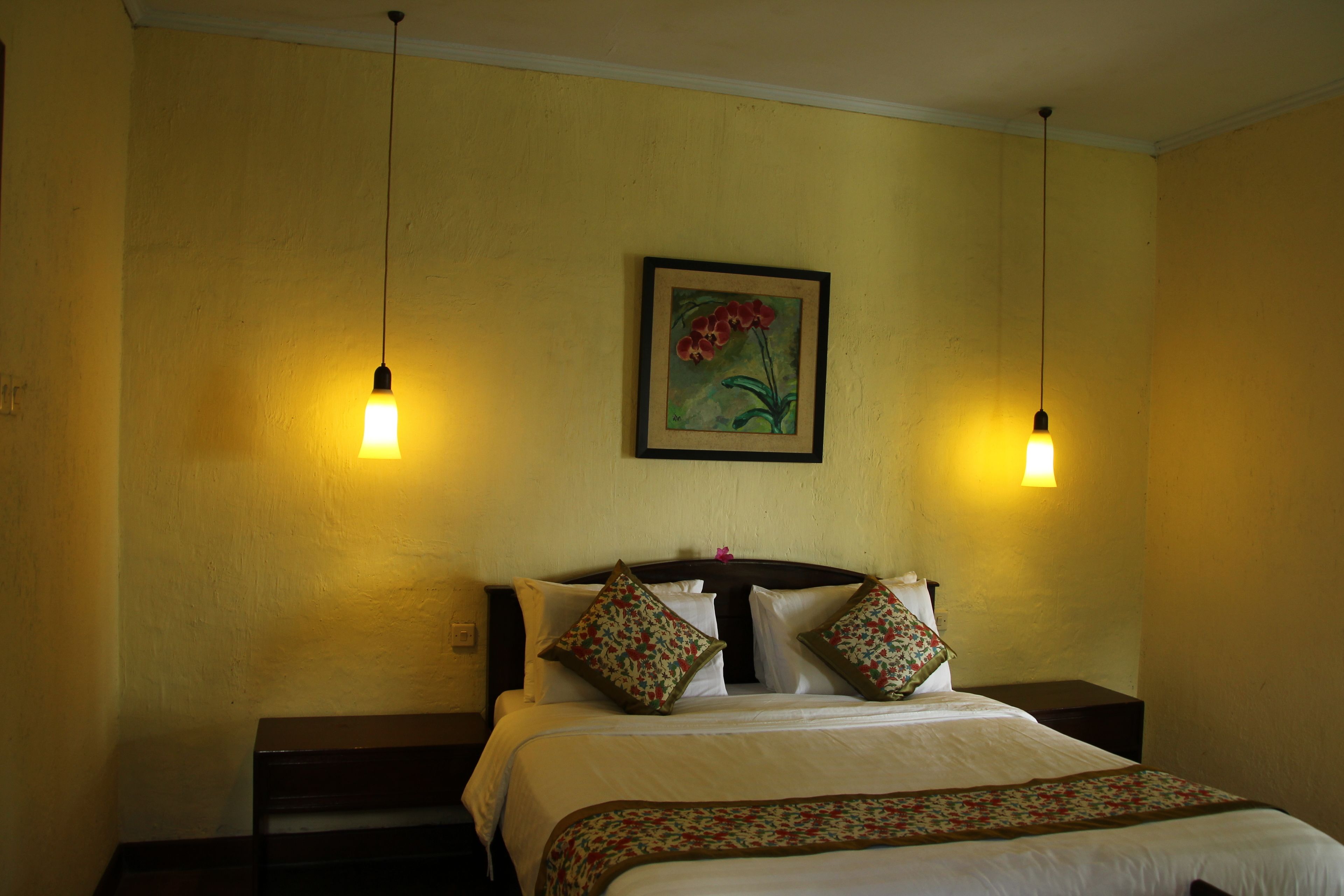 A hotel room with a bed, two bedside tables, and two hanging light fixtures.