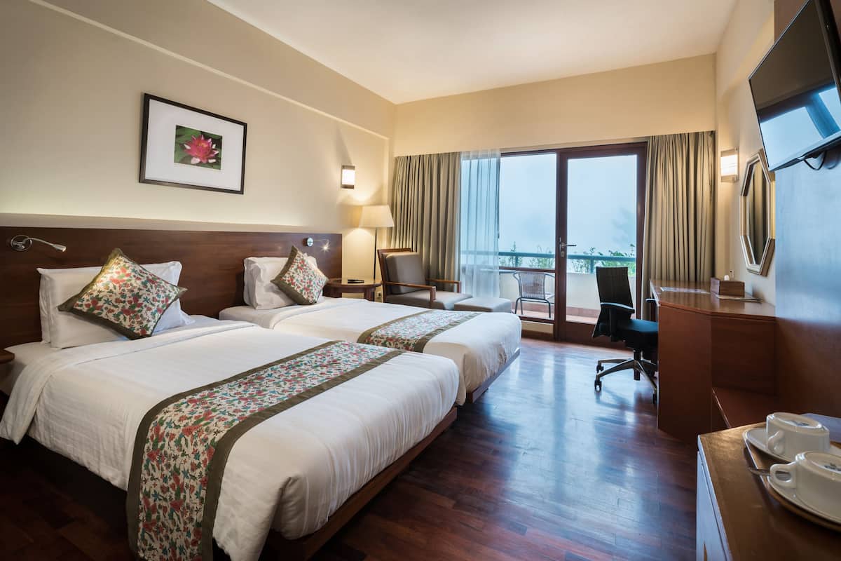 A hotel room with two beds, a desk, a chair, a TV, and a balcony with curtains.
