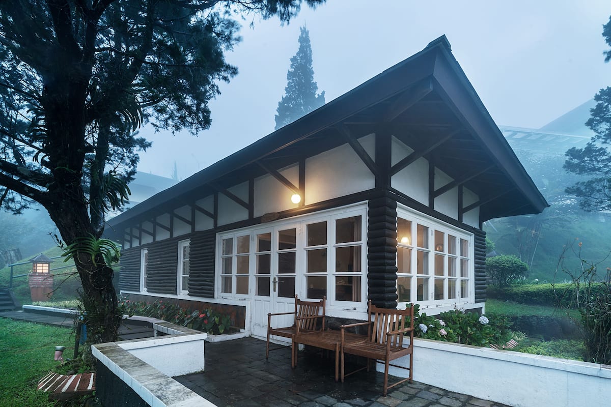 A modern house with a large porch, wooden chairs, and a view of the surrounding landscape.
