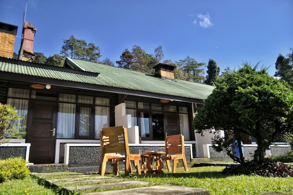A building with a green roof, wooden chairs, and a small table in the front yard.