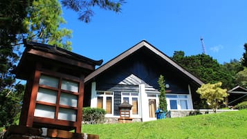 Ein traditionelles Holzhaus mit geneigtem Dach, einer kleinen Holzlaterne und einem steinernen Weg, der zum Eingang führt.