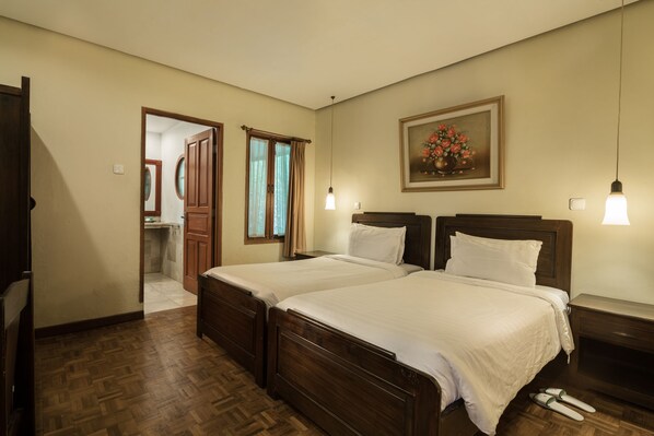A hotel room with two wooden beds, a nightstand, a framed floral artwork, and a wooden floor. - Puncak Pass Resort (Cipanas)