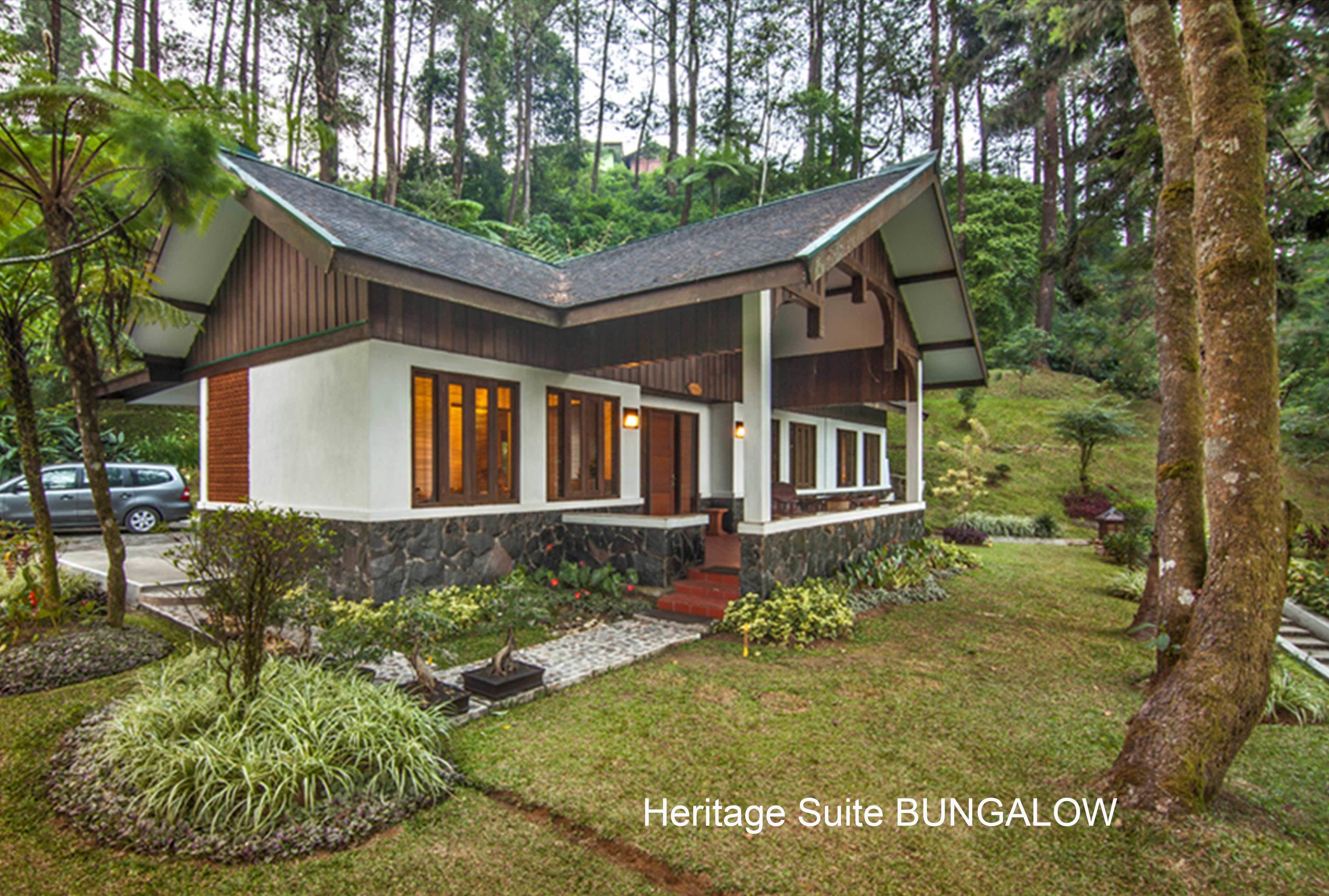 Un bungalow à la façade en pierre, agrémenté de détails en bois et doté d’un porche, le tout entouré d’une végétation luxuriante.