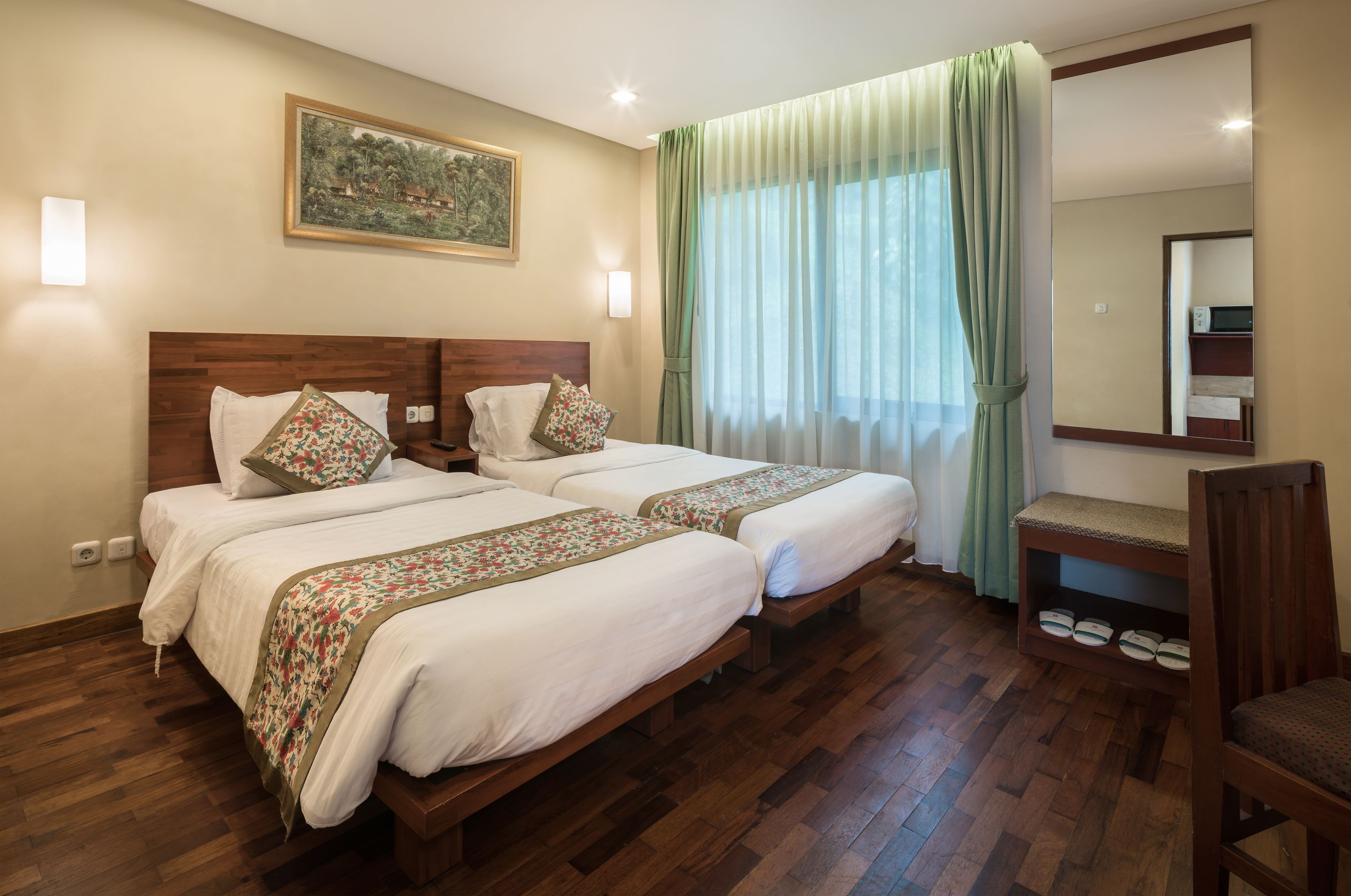 A hotel room with two beds, wooden headboards, a small desk, and a mirror.