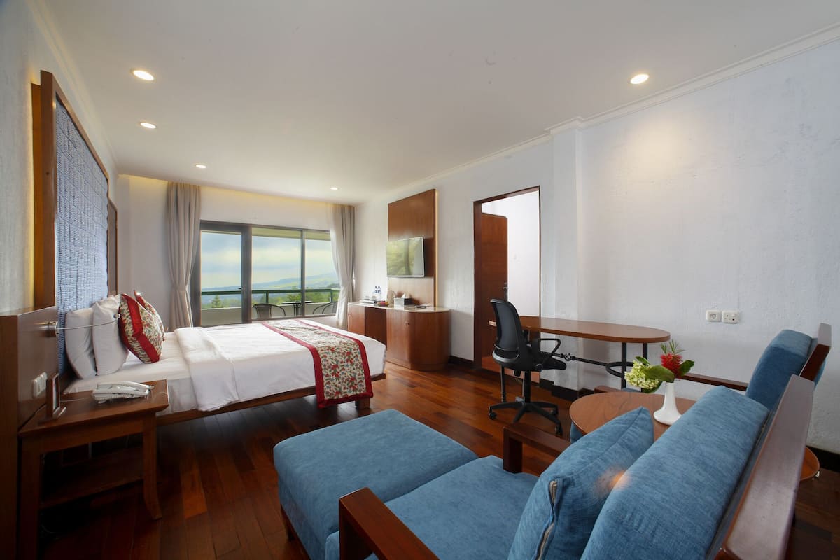 A hotel room with a bed, a desk, a chair, a sofa, and a balcony with a view.