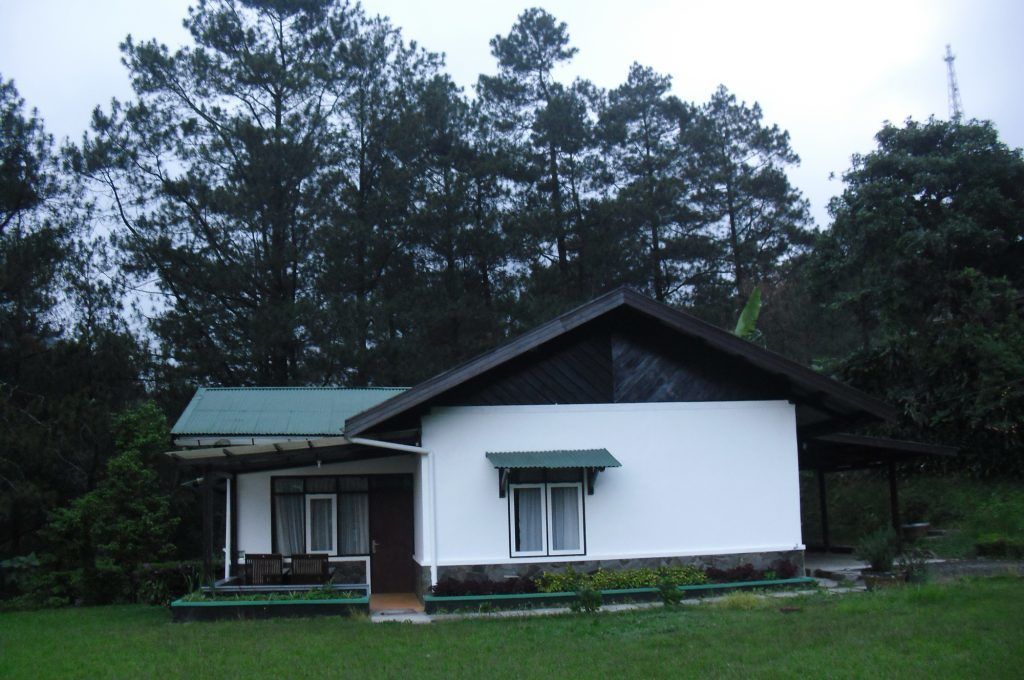 A single-story building with a sloped roof, a porch with a bench, and a small garden area.
