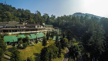 A multi-story hotel with a green roof, surrounded by lush greenery and a mountain in the background.