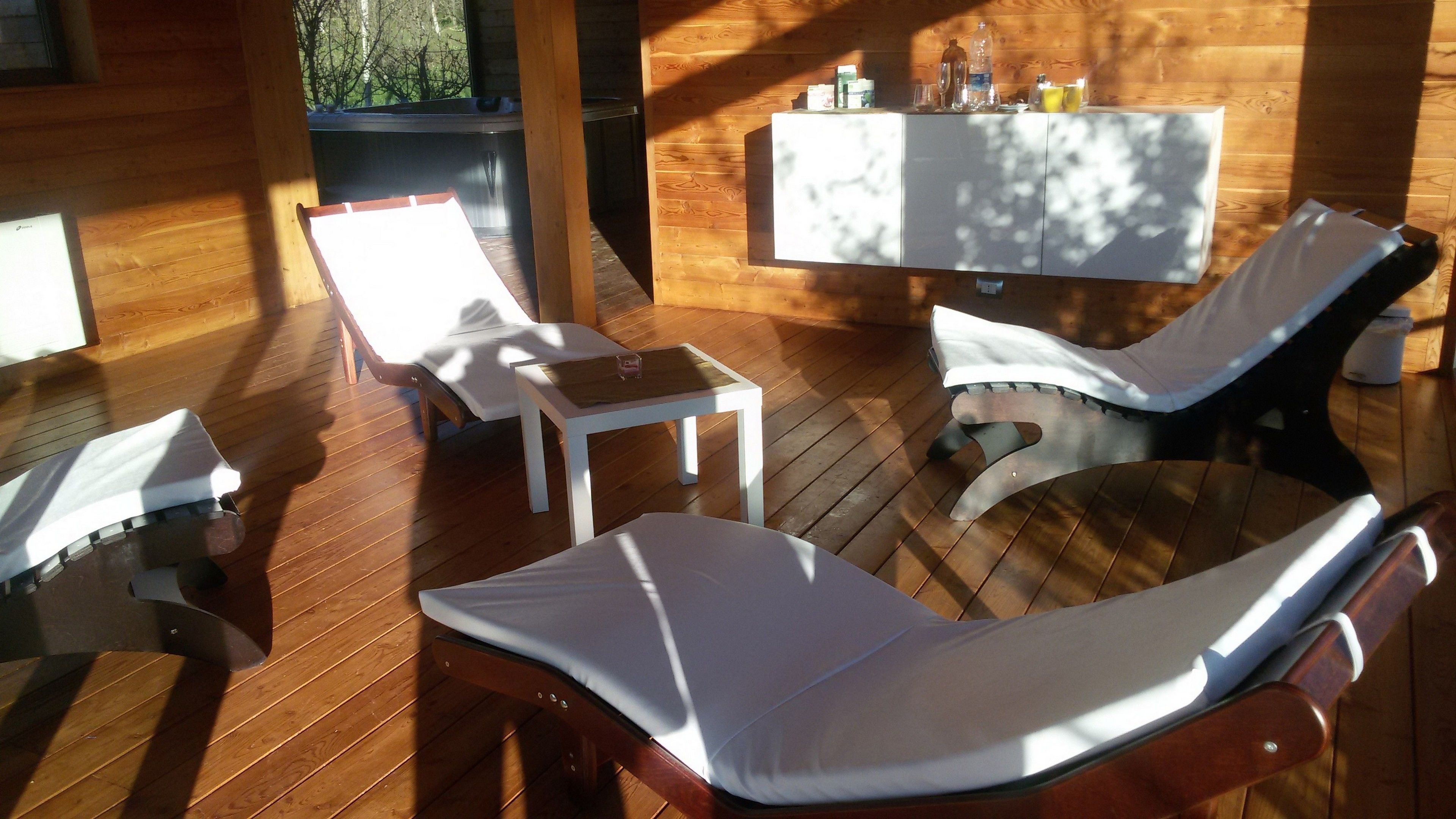 A wooden deck with two lounge chairs and a small table, a hot tub, and a table with various items.