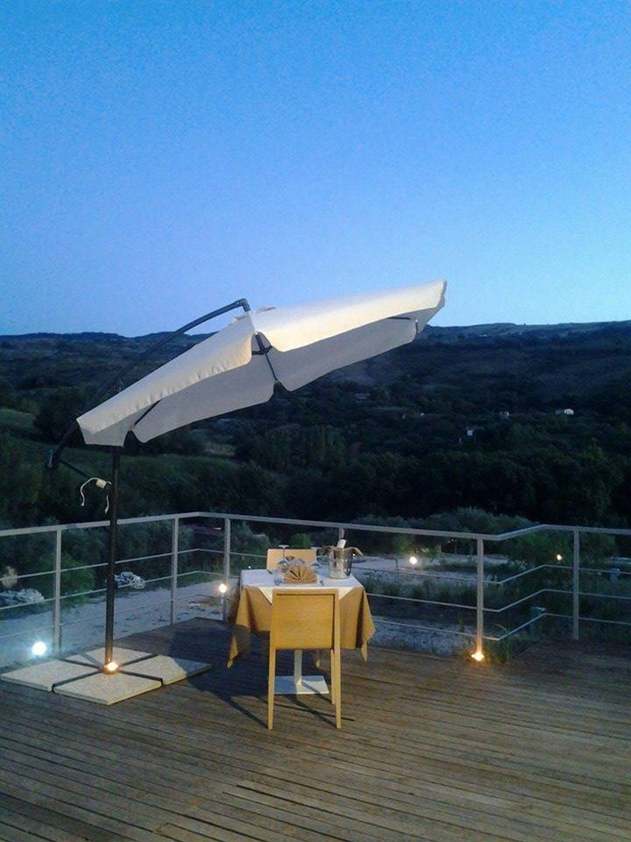 An outdoor dining area with a table and chairs under a large umbrella, overlooking a scenic landscape.