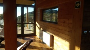 Een houten hut met grote ramen, een balkon en uitzicht op een bergachtig landschap.