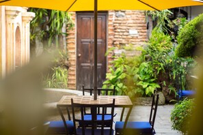 An outdoor patio with a table and chairs, a yellow umbrella, and a stone wall with greenery. - La Villa Serena  (Antigua Guatemala)