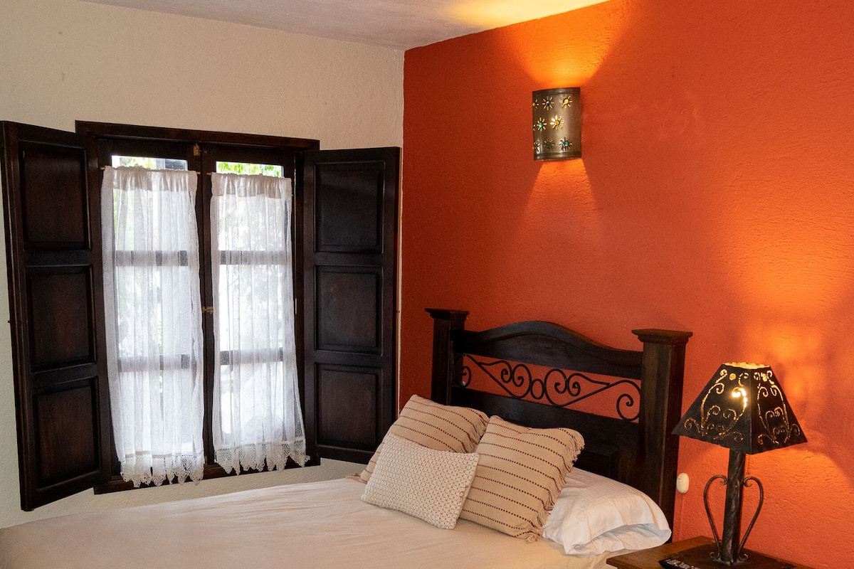 Una cama doble con cabecera de madera, una mesita de noche con lámpara y una ventana con cortinas.