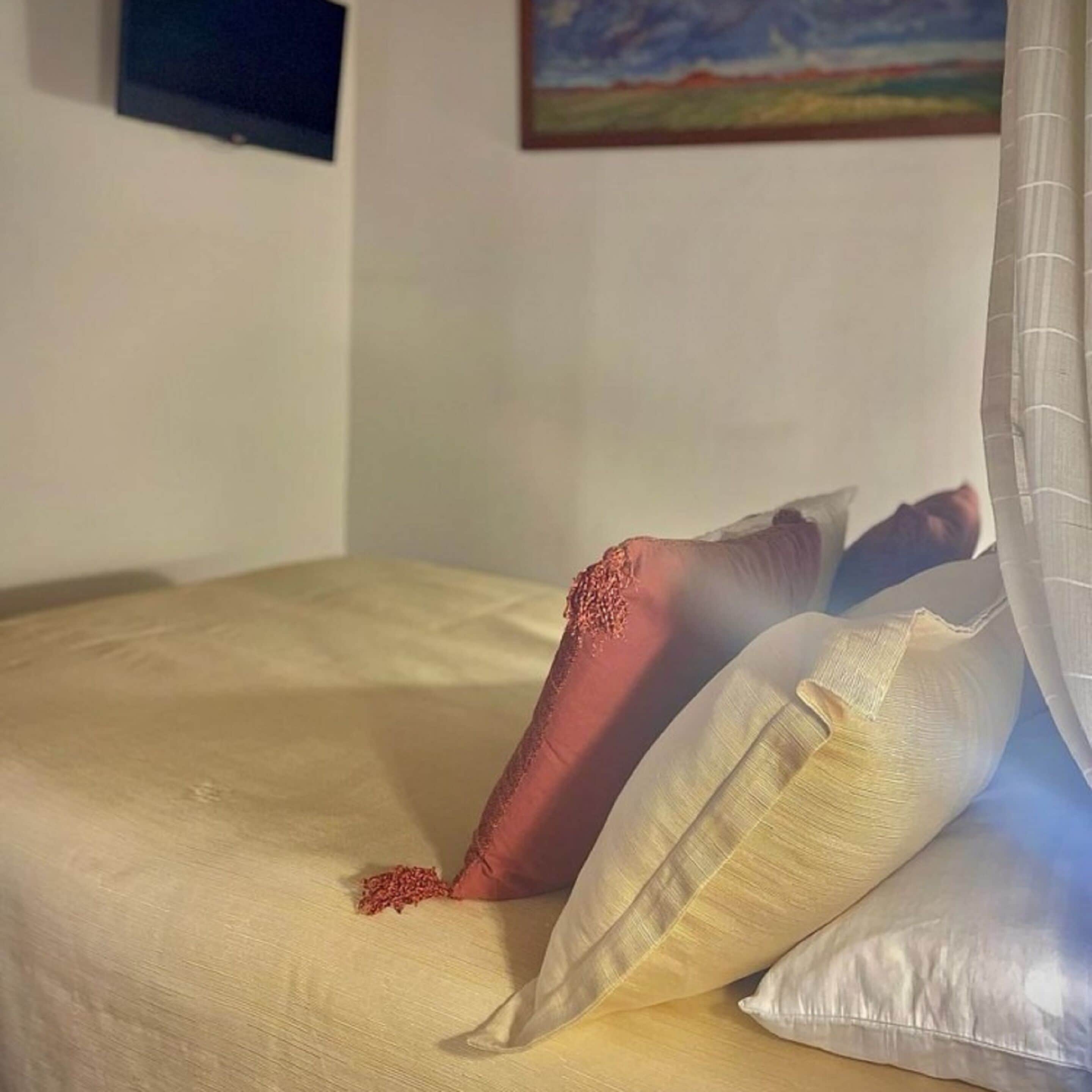 Uma cama com um cobre-leito bege, um travesseiro vermelho e um travesseiro branco.